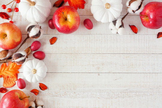 Red and white theme autumn corner border with apples and pumpkins on a white wood background. Copy space.