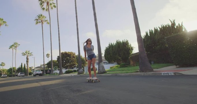 Attractive adventurous girl skateboarding down palm tree lined street at sunset 