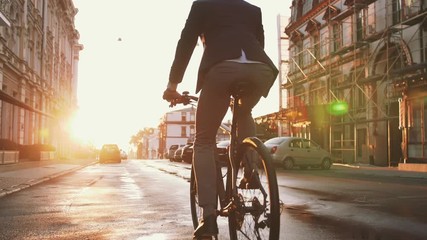 Handsome young man driving his bicycle on the street in city center during sunrise - Powered by Adobe