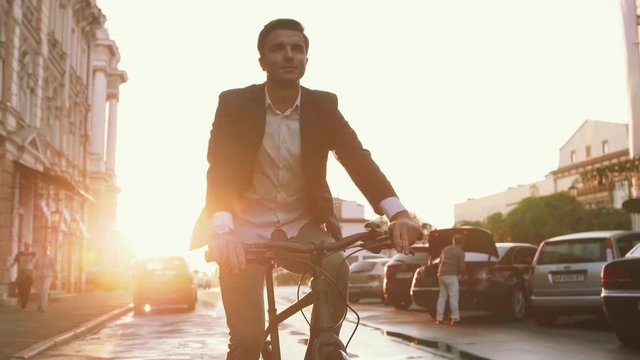 Handsome young man driving his bicycle on the street in city center during sunrise
