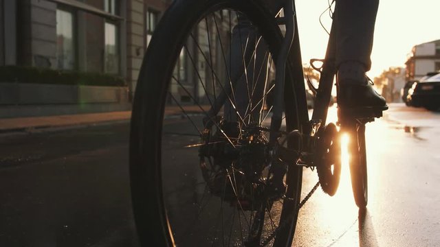 Close up shot of young man driving his bicycle on the street in city center during sunrise in sun beams