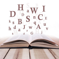 Opened Book on Wooden Table Against White Background with Letters Flying