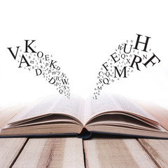 Fototapeta premium Opened Book on Wooden Table Against White Background with Letters Flying