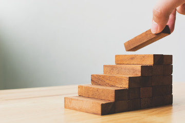 Hand arranging wood block stacking as step stair. Ladder career path concept for business growth success process