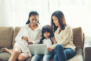 Fototapeta premium happy Young family sitting on sofa and looking at laptop in home