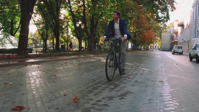 Handsome young man driving his bicycle on the street in park in city center during sunrise, slow motion