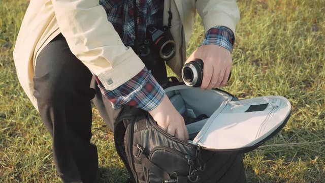 Photographer changing lenses of photo equipment in backpack.