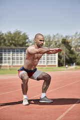 Fototapeta na wymiar one young muscular man, shirtless, side view, squat exercise. outdoors, sports venue, running tracks.