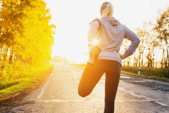 Fitness woman runner stretching legs before run on the road.