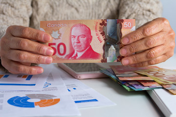 Paper notes from Canada. Dollar. Retired woman holding bill on desk office.