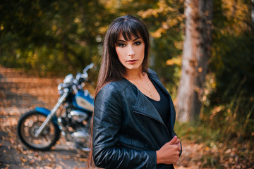 Fototapeta na wymiar The girl in a black leather jacket with long hair. Motorcycle in the background