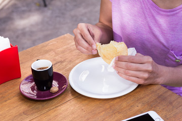 Detail of woman holding pao de queijo and cup of coffee. Brazilian food for a afternoon snack. Outdoors.