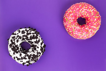 Donuts pink and chocolate on purple background top view