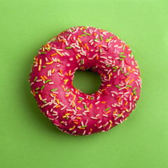 Pink donut on a green background top view in a square