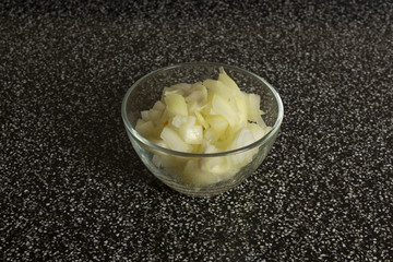 A glass plate of sliced white onion on the granit surface of a kitchen table