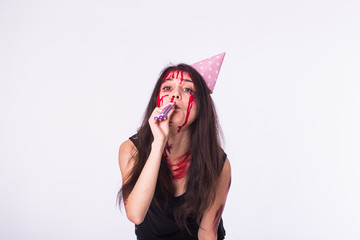 Halloween and carnival concept - young woman with blood on face celebrate holidays with whistle