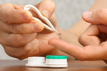 hands with tweezers take contact lenses