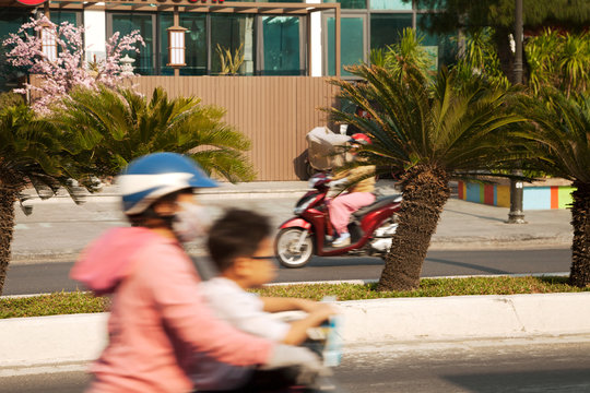 Two motorbikes in motion on a quiet sunny road. Blurry mother and a child on riding a bike on an Idyllic tropical city street with palm trees