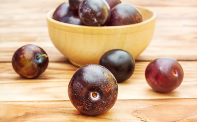 Wooden bowl with plums on the table.