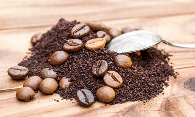 Heap of ground coffee and coffee beans with spoon on the table.