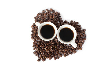 Two cups of black coffee and a heart made of coffee beans on white backgroung isolated top view