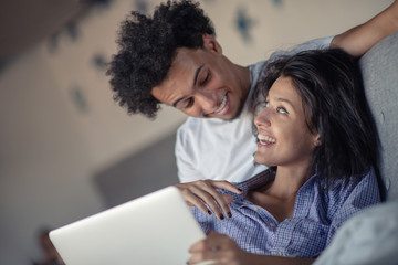 Young attractive diverse couple browsing internet, using laptop computer, smiling.