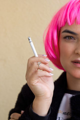 young woman in a pink wig   holds cigarette  in her hand portrait, close up cigarette in a hand half of a face