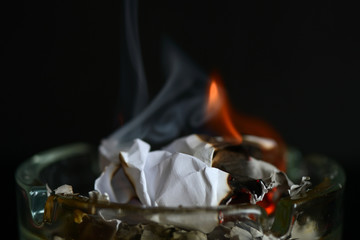 A piece of paper burning in a glass ashtray close up