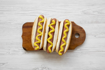 Hot dog with yellow mustard on wooden board on white wooden table, view from above. Flat lay, overhead, top view. Closeup.