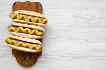 Hot dog with yellow mustard on wooden board on white wooden background, overhead view. Top view,...