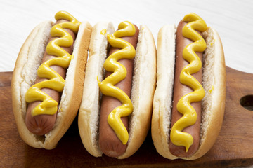 Hot dog with yellow mustard on wooden board on white wooden background, side view. Close-up.