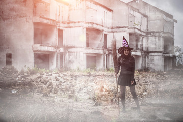 Plakat Halloween young woman in witches hat stands and a broom in hand on a black building background, Fashion glamour art design.