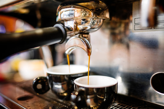 Close-up of espresso pouring from coffee machine into cups. Professional coffee brewing, barista details
