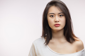 Fototapeta premium Confident sensual young Korean woman with long hair, dressed in white t-shirt looking at camera over white background. Youth and Beauty concept
