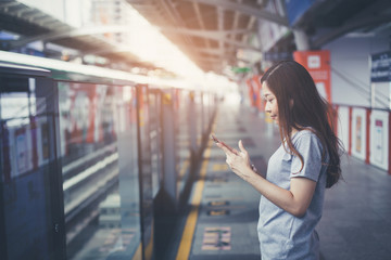 Young woman waiting for electric trains on the platform and using the smart phone to find the route.