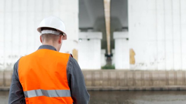 A man inspector examines the condition of the columns of the bridge across the river and marks the shortcomings, engineering