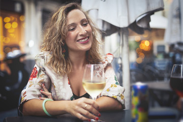 mid aged blonde woman drinking white wine and smiling on a bar table with her friends. 40s Togethernes concept.