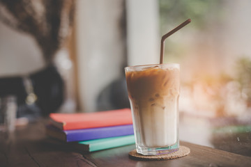 Close up of a cup of cappuccino or latte coffee with a  white foam on a wooden background in a cafe, Book on the table.