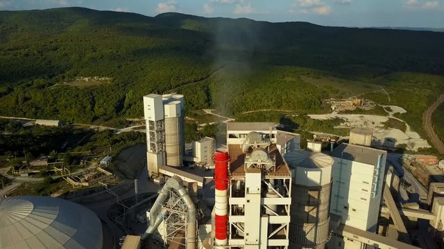 Aerial view of cement factory, large industrial building in the mountains. Concept of cisterns, pipes, metal structures, concrete production. Daytime footage with a beautiful blue sky.