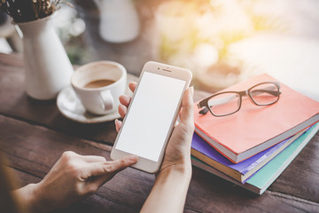 Mockup portrait of a woman hand holding a  cell phone with blank screen and a cup of coffee in cafe.