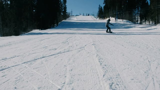 Teenage boy of 12 years in grey suit sliding on a snowboard from snow descent next sky lift. Front view.