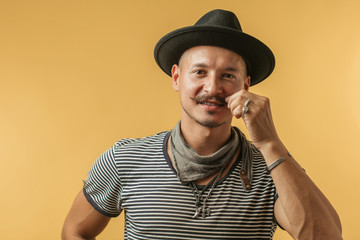 Happy handsome caucasian man with moustache wearing hat and stripped shirt isolated over yellow...