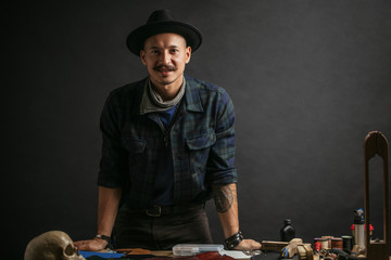 Portrait of handsome Leather goods craftsman in stylish hat doing handbags and leather accessories...