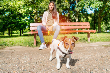 Dog Jack Russell Terrier on a leash with curiosity and great interest in looking forward, licking tongue muzzle, mistress sitting on a bench in the park