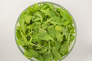 Fresh arugula salad in a glass bowl isolated on white background. Top view