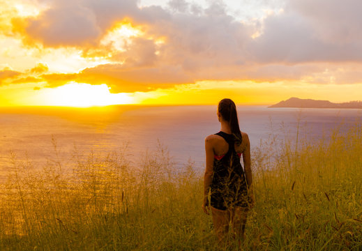 Young female standing on a hill looking down at the beautiful sunset. 