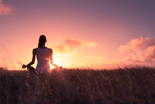 Young woman meditating outdoors at sunset. 