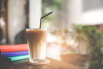 Close up of a cup of cappuccino or latte coffee with a  white foam on a wooden background in a cafe, Book on the table.