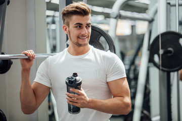 Fototapeta na wymiar Athlete man having a snack with protein cocktail in shaker over gym machine background