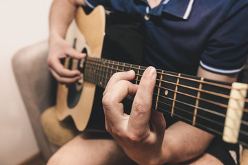 Fototapeta na wymiar Man at home is playing the guitar. Guys hands are taking the chord on strings. Music making lifestyle concept. Free time hobby for everyone. Retro guitar photo.